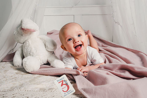 A little baby lays on a bed with a toy rabbit and smiles